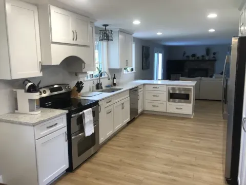 Modern kitchen with white cabinets, stainless steel appliances, and light wood flooring.