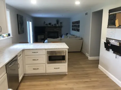 Modern kitchen with white cabinets, a built-in microwave, and view into a living room area.