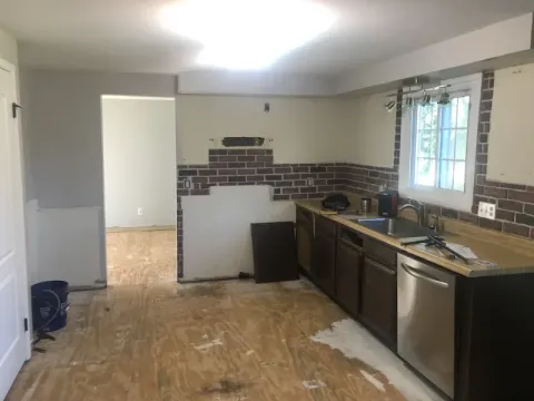 Partially remodeled kitchen with bare plywood floor and missing cabinets, backsplash exposed.