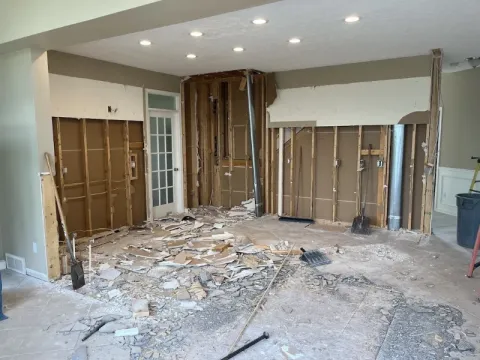 Room under renovation with exposed wall studs, debris on the floor, and tools scattered around.