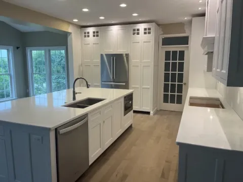 Modern kitchen with white cabinets, stainless steel appliances, and large windows.