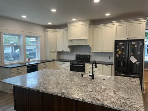 Modern kitchen with white cabinets, a large granite island, and stainless steel appliances.