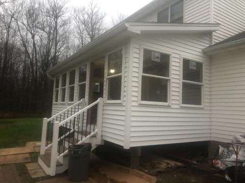 White house with enclosed porch, steps with railing, and trash can by the entrance on a cloudy day.