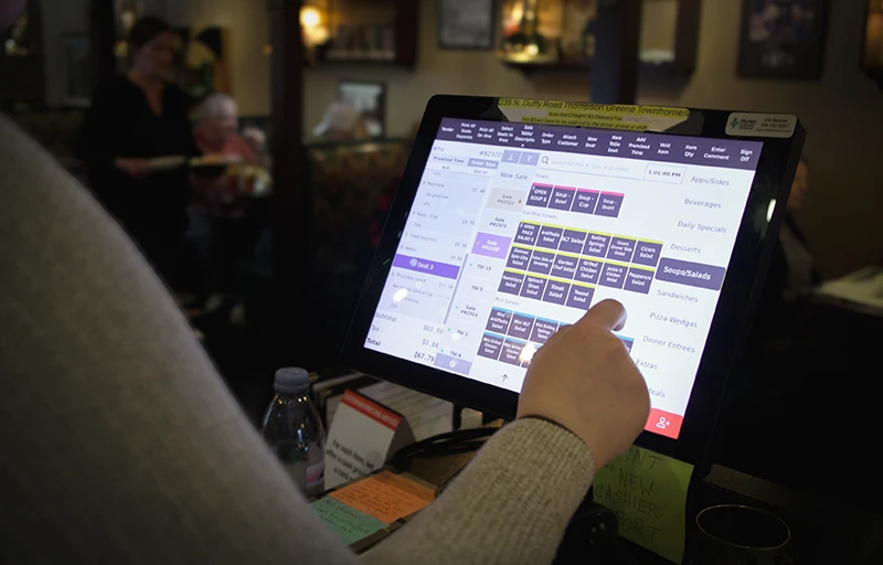 A person uses a touchscreen point-of-sale system at a restaurant counter.