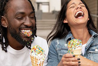 Two people laughing and enjoying ice cream cones covered with colorful sprinkles.