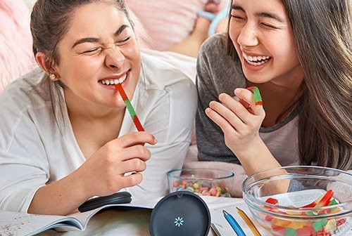 two young girls laughing and eating gummy worms