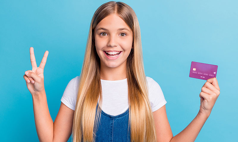 Teen girl holding a credit card and smiling while giving the peace sign.