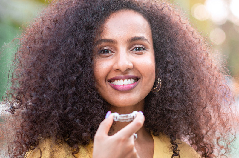 A smiling woman with curly brown hair holding a set of clear braces.