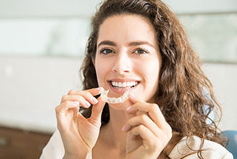 Woman smiling and holding a clear dental aligner in her hands, ready to place it in her mouth.