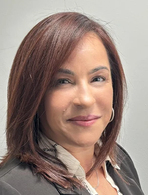 Person with brown hair wearing a black jacket over a white blouse, smiling at the camera.